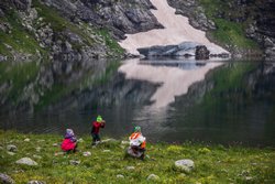 Дети на берегу озера Голубое разбивают камни, добывая красивые кусочки кварцитов на память.